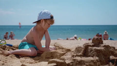 Smiling boy sitting and play with sand on the beach Stock Footage 138257002
