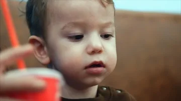 A smiling boy sitting next to his mother drinks milk through a red straw from a Stock Footage 86006541