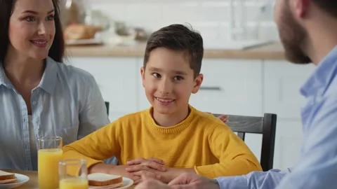 A smiling boy is sitting at the table with his mother and father. The boy is Stock Footage 240059213