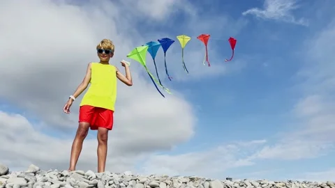 Smiling boy stand on pebble beach holding many colorful kites Video stock 234977520