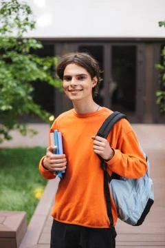 Smiling boy standing with backpack and books in hand and happily looking in Stock Photos