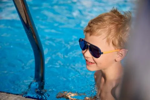 Smiling boy in sunglasses swam up to the steps in the pool to climb Stock Photos
