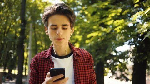 Smiling boy using mobile phone listens to music in headphones walk guy business Video stock 92049020