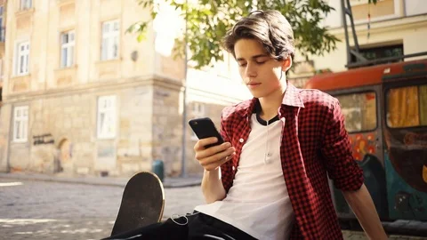 Smiling boy using a mobile phone sitting keeps skate smile guy business fashion Stock Footage 92049947