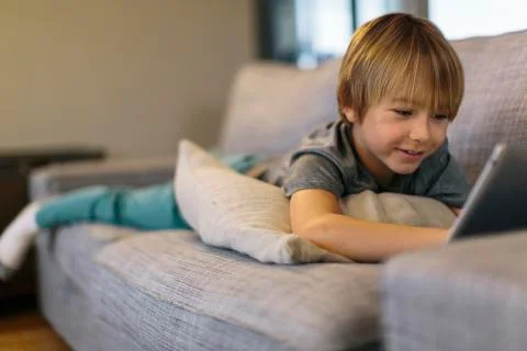 Smiling boy using tablet computer while lying on sofa at home Stock Photos