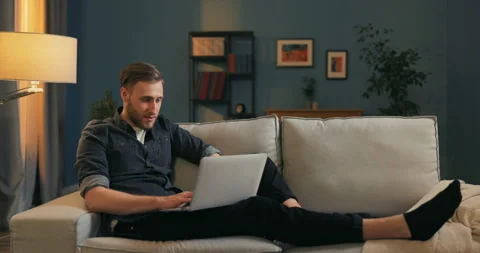 Smiling boy works remotely in his own living room on his couch, holds his laptop Stock Footage 160514814