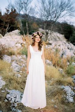 Smiling bride in a multi-colored wreath stands on a mountain among the stones Stock Photos