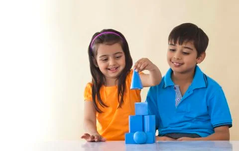 Smiling brother and sister stacking geometric shapes over colored background 스톡 사진