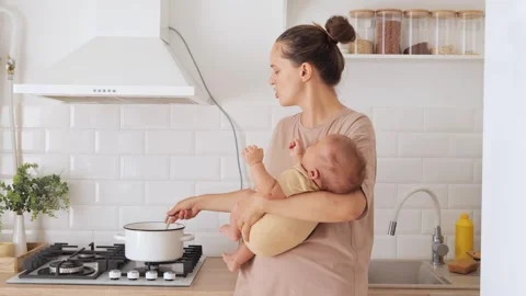 Smiling brown haired mom carrying her baby boy while cooking dinner balancing Stock Footage 291272806