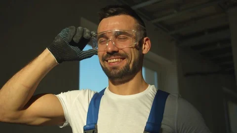 Smiling builder stands and puts off protective glasses, slow motion Stock Footage 124841538