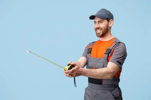 Smiling builder worker holding and looks on measuring tape tool. Studio shoot Foto stock