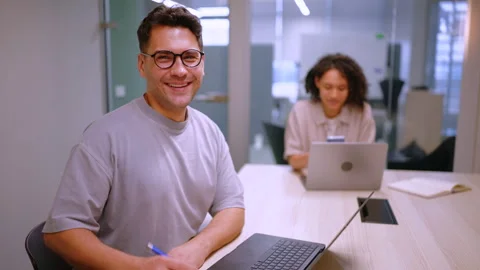 Smiling businessman adjusting glasses while working on laptop Vídeos de archivo 342906050