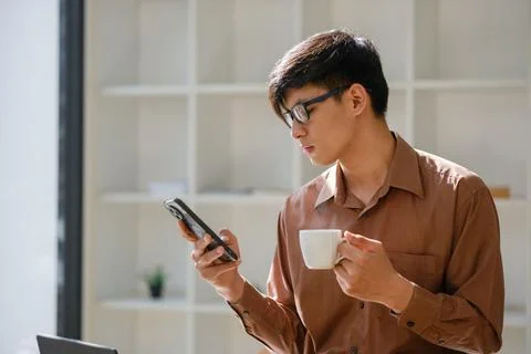 Smiling businessman checking phone while holding coffee during break Stock Photos