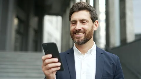 Smiling businessman in formal suit is using a mobile phone while standing  Stock Footage 301634643