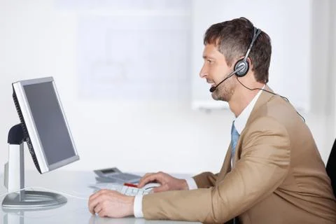 Smiling businessman with headset looking at computer screen Stock Photos