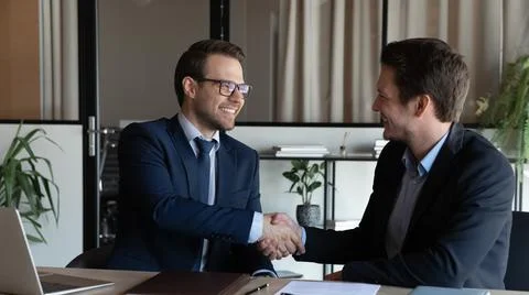 Smiling businessman manager shaking satisfied client hand at meeting Stock Photos
