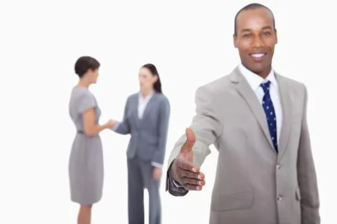 Smiling businessman offering his hand with hand shaking colleagues behind him Stock Photos