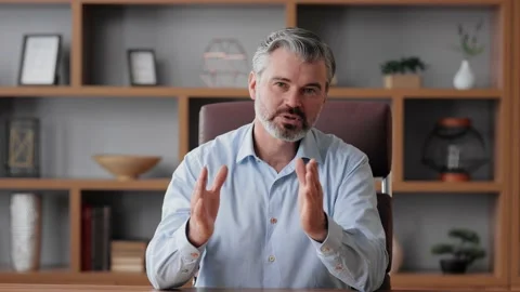 Smiling businessman talking to web camera sitting in office. Recording vlog Stock Footage 198429665