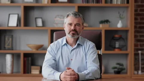 Smiling businessman talking to web camera sitting in office. Recording vlog Stock Footage 217049246