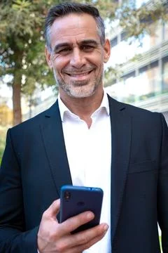 Smiling businessman using an application on his smartphone and standing.Vertical Stock Photos