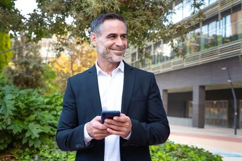 Smiling businessman using an application on his smartphone and standing outdoors Stock-Fotos