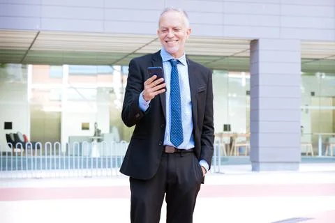 Smiling businessman using an application on his smartphone and standing.Vertical Stock-Fotos