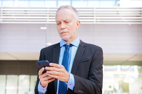 Smiling businessman using an application on his smartphone and standing. Stock Photos
