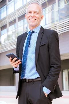 Smiling businessman using an application on his smartphone and standing.Vertical Stock Photos