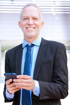 Smiling businessman using an application on his smartphone and standing.Vertical Stock Photos