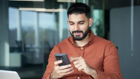 Smiling businessman is using browsing mobile phone while sitting at workplace  Stock Footage 305655327