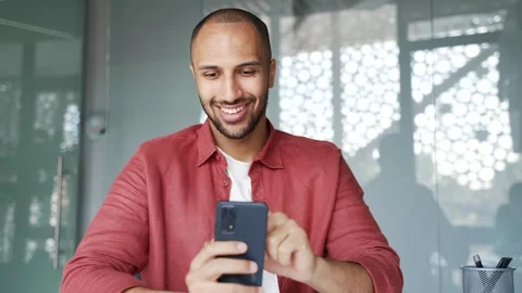 Smiling businessman is using browsing mobile phone while sitting at workplace  Vidéo 340880191