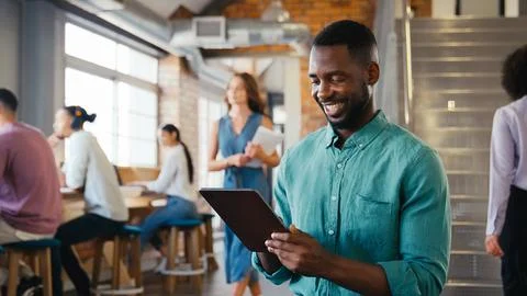 Smiling Businessman Using Digital Tablet Working In Busy Modern Open Plan Office Stock Photos