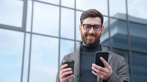 Smiling businessman using smartphone drinking coffee walking in office district Stock Footage 163300304