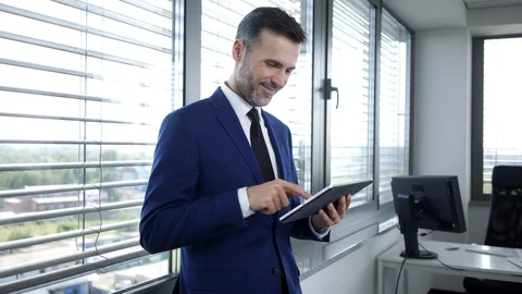 Smiling businessman using tablet and leaning against office windown Video stock 114813015