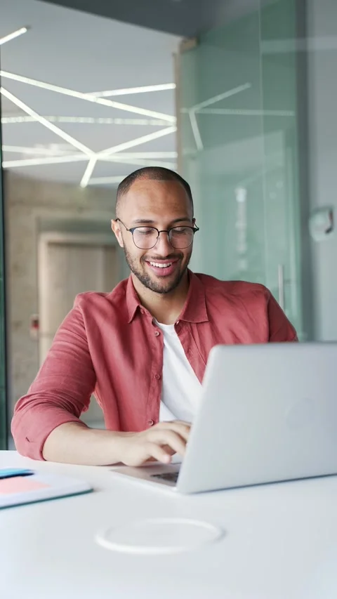 Smiling businessman working on a laptop while sitting at a workplace in a modern Vídeos de archivo 340880151