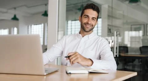 Smiling businessman writing down notes while working on a laptop Stock Photos