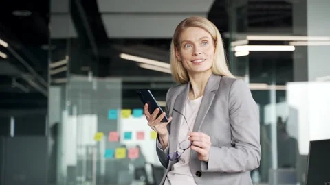 Smiling businesswoman in a jacket is using mobile phone while standing Stock Footage 297775624