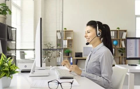 Smiling call center operator with headset working at computer in modern office Stock Photos