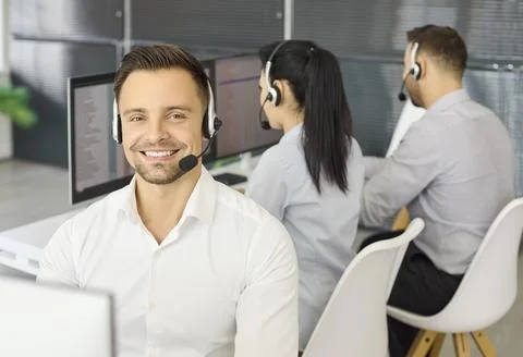 Smiling call center operator with headset at computer in modern office workspace Stock Photos