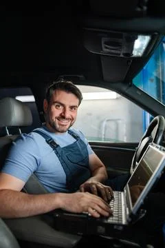 Smiling car mechanic using laptop for diagnostics inside a car Stock Photos