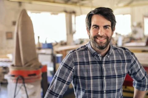 Smiling carpenter standing alone in his large woodworking studio Stock Photos