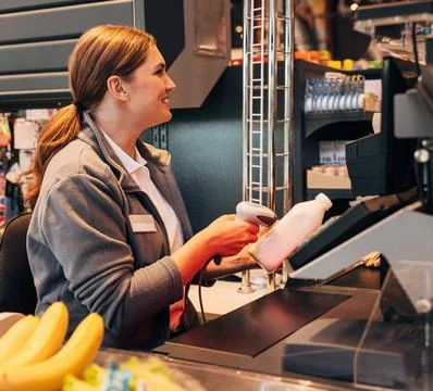 Smiling cashier using a barcode scanner on a bottle of milk Stock-Fotos