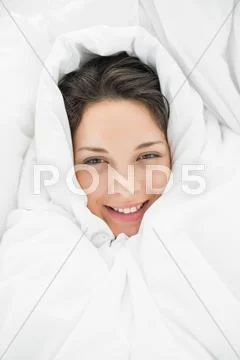 Smiling casual brunette wrapped up in her duvet Stock Photos