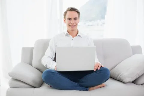 Smiling casual young man using laptop on sofa Stock Photos