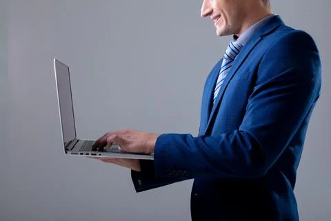 Smiling caucasian businessman using laptop, isolated on grey background Stock Photos