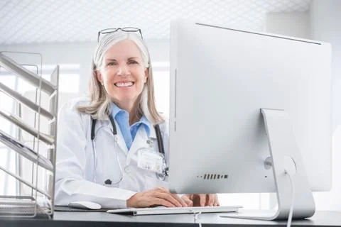 Smiling Caucasian doctor using computer at desk Stock Photos