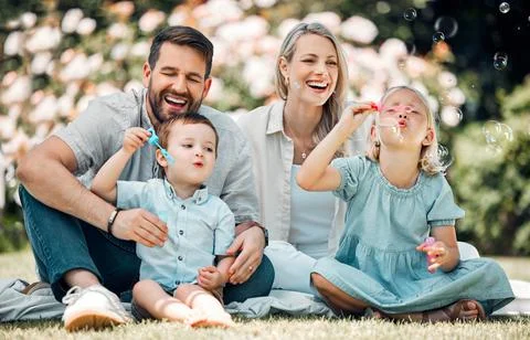 Smiling caucasian family blowing soap bubbles for fun while relaxing together in Stock Photos