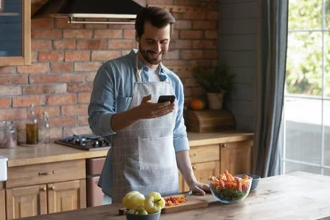Smiling Caucasian man cook with recipe on cellphone Stock Photos