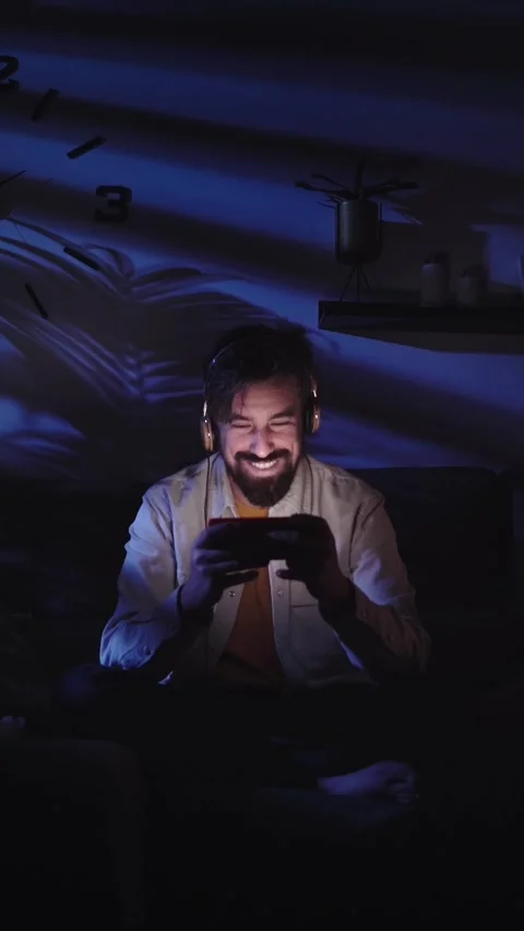 Smiling Caucasian man looking cell phone in living room with headphones. Young Stock Footage 275182108