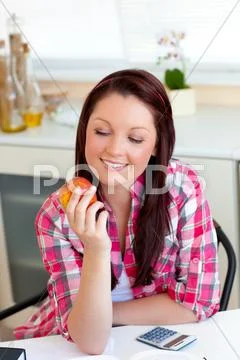 Smiling caucasian woman holding an apple sitting in the kitchen Stock Photos